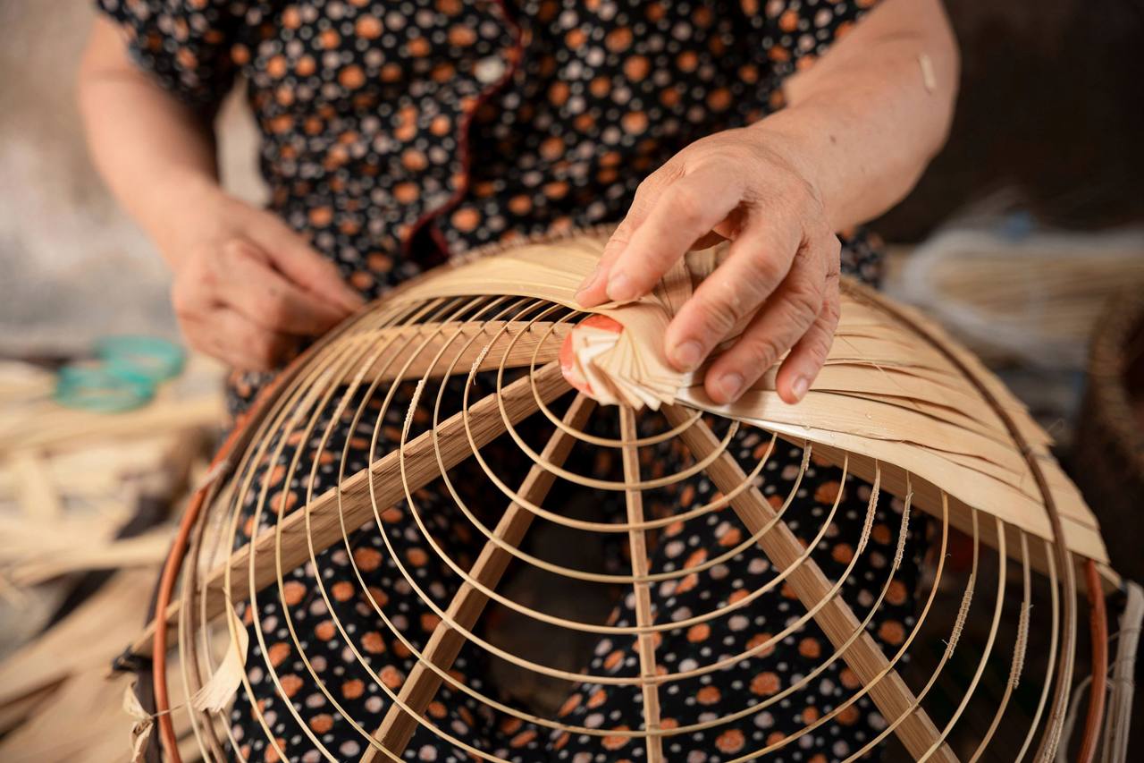 Đôi tay người thợ đang đan nan tre quanh một khung tròn hình chao đèn, ở một làng nghề tại Hà Nội